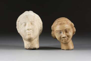 ZWEI FRAUENKÖPFE Römische Kaiserzeit Marmor, plastisch gearbeitet. H. 12 cm bzw. 14 cm. Jeweils portraithafte Darstellung einer unbekannten Frau mit welligem Haar. Part. min. best. Provenienz: Deutsche Privatsammlung.