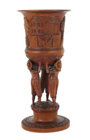 Pokal wohl Brienz/Schweiz, um 1900, Holz geschnitzt, runder blattwerkentourierter Stand, der Schaft in Form dreier vollplastischen die Kuppa haltenden Figuren, die 3 Urkantone symbolisierend, Wandung umgehend mit bäuerlichern Szenen, H: ca - photo 1