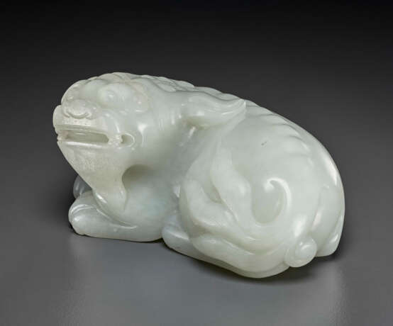 A FINELY CARVED PALE GREYISH-WHITE JADE FIGURE OF A RECUMBENT MYTHICAL BEAST - фото 1