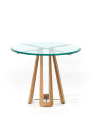 Table with circular crystal top, shaped light wood legs and brass connecting elements