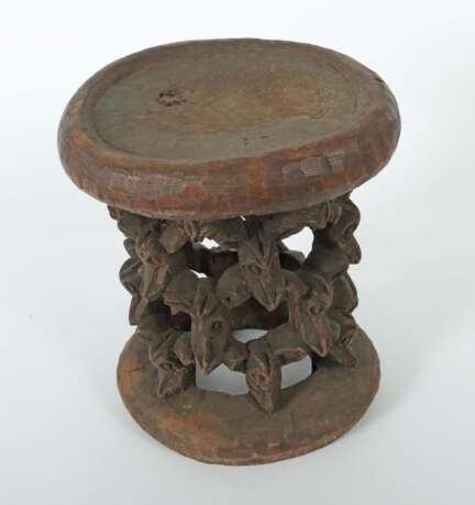 Afrikanischer Hocker aus einem Stück Holz geschnitzt, mit ringförmigem Stand und gitterartig angeordneten Miniaturmasken als Stützen der leicht ovalen Sitzfläche - фото 2