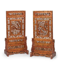 Zwei große Tischstellschirme aus Holz, geschnitzt teilweise in Durchbruch mit Darstellung von berittenen Kriegern in Gebirgslandschaft und Glückssymbolen, beidseitig Rotlack und partielle Vergoldung