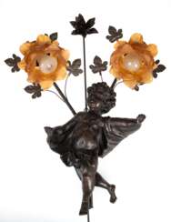 Wandlampe mit Putti, 2-flammig, Gußmasse/ Eisen, dunkelbraun patiniert, 2 floral gestaltete Leuchterarme mit braunen, floralen Glasschirmen, Gebrauchspuren, elektrifiziert, H. 56 cm