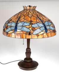 Tischlampe im Tiffanystil, Ende 20. Jh., 2-flammig, auf rundem, gegliedertem Eichenfuß, Schirm aus beige/braunem Kunstglas, Rand umlaufend mit hellblauen Libellen, H. 65 cm, Dm. 53 cm