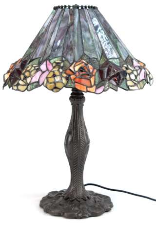 Tischlampe im Tiffanystil, 2. Hälfte 20. Jh., 2-flammig, auf rundem, dunkel patiniertem Metallfuß mit Floralrelief, Schirm aus lila/beigen Kunstglas mit bunter Blumenkante, H. 59 cm, Dm. 45 cm - photo 1