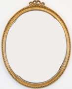 Möbel. Spiegel, oval, im goldenem Holzrahmen mit Reliefdekor und Schleifenbekrönung, mit facettiertem Glas, 70x56 cm
