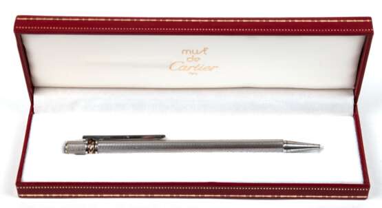 Kugelschreiber von Cartier, sog. "Must de Cartier", silberfarben, teilw. farbig emailliert, Korpus mit feinem Netzdekor, oberhalb eingelassener Trinity-Ring, L. 13,5 cm, originales Lederetui - Foto 1