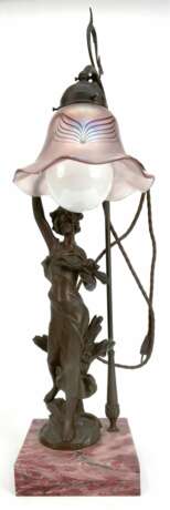 Tischlampe, figürlich "Junge Frau mit schwingendem Gewand und Blumen im Arm", Weißmetall braun patiniert, 1-flammig, blütenförmiger Lampenschirm aus irisierendem Glas höhenverstellbar, auf quadratischem Marmorsockel, Ges.-H. bis ca. 80… - Foto 1
