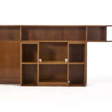 Custom-designed low cabinet, consisting of two bodies, one symmetrical central body with open compartments, the other asymmetrical with a door cupboard and three open compartments. 1960s. Solid and veneered wooden frame. (238.5x107.5x59 cm.) (defects - Foto 1