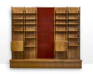 Large custom-designed bookcase made of solid wood and veneer, consisting of three bays, the central one of which is set up with a backdrop covered in red fabric, two drop-down cabinets, twenty shelves, and a base. How, 1970s. (344x300x45 cm.) (slight