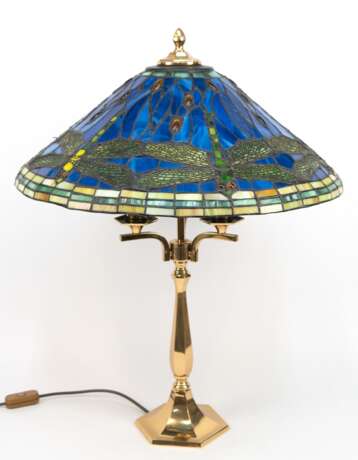 Tischlampe im Tiffanystil, 2. Hälfte 20. Jh., 3-flammig, gegliederter Messingfuß auf sechseckigem Stand, Schirm aus farbigem Kunstglas mit umlaufendem Libellendekor, H. 70 cm, Dm. 53 cm - фото 1