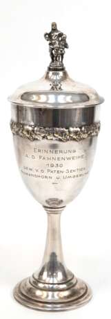 Deckelpokal, versilbert, auf gestuftem Rundfuß, Deckel mit figürlicher Bekrönung, umlaufende Weinlaubrelief, Widmungsgravur "Erinnerung a. d. Fahnenweihe 1930...", H. 34 cm - Foto 1