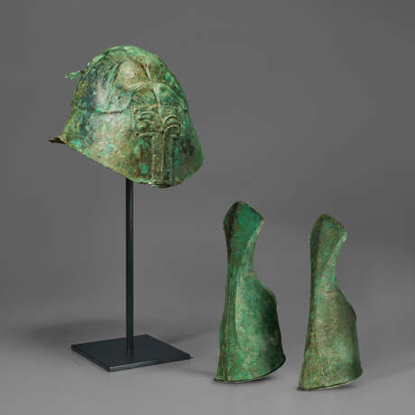 A GREEK BRONZE APULO-CORINTHIAN HELMET AND PAIR OF ANKLE-GUARDS - photo 1