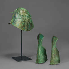 A GREEK BRONZE APULO-CORINTHIAN HELMET AND PAIR OF ANKLE-GUARDS