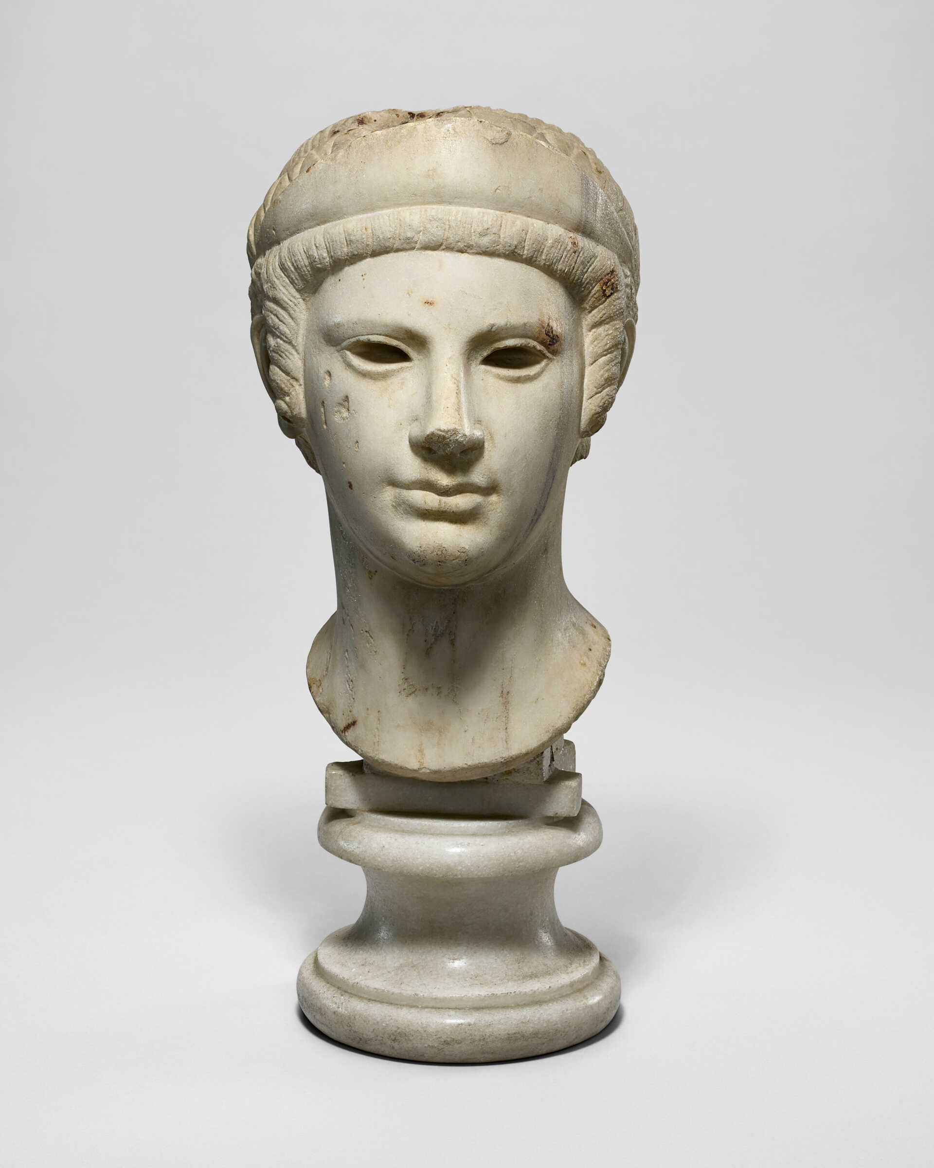 A ROMAN MARBLE ARCHAISTIC HEAD OF A GODDESS