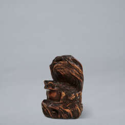 A CARVED WOOD NETSUKE OF A FROG SITTING IN THE SHADE OF A TREESTUMP