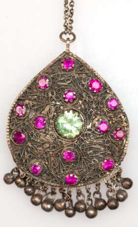 Buddhistischer Amulett-Anhänger, Metall mit 14 Rubinen von je ca. 1 ct. und Kiwi-Topas besetzt, tropfenförmiger Anhänger rücks. mit Buddha-Relief, beweglich anhängende Kugel (1x fehlt), L. mit Öse L. 9 cm - фото 1