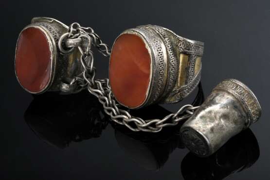Zwei diverse durch Gliederkette verbundene turkmenische Ringe mit Fingerhut "Kökenli Yüsük", Ringkopf mit großen ovalen Karneole in ornamentaler Fassung auf spitz zulaufender Ringschiene, Silber partiell vergol… - photo 1