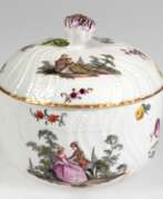 Porcelain products. Meissen-Dose, Schwertermarke um 1750, Form Neubrandenstein, Wandung und Deckel mit polychromer Watteau- und Blumenmalerei, Goldrand, plastische Blüte als Deckelbekrönung, Deckelrand und Blüte bestoßen, Ges.-H. 11 cm, Dm.…