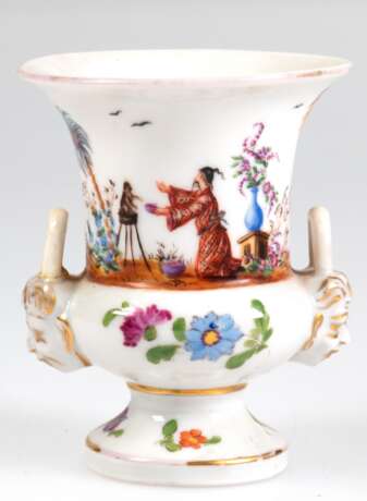 Kleine Kratervase, ungemarkt, wohl Thüringen um 1900, umlaufende Chinoiserie-Malerei in der Art von Meissen, darunter polychrome Blumemmalerei, seitl. Maskarone mit Golddekor als Henkel (1x repariert), Goldränder (berieb… - Foto 1