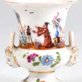 Kleine Kratervase, ungemarkt, wohl Thüringen um 1900, umlaufende Chinoiserie-Malerei in der Art von Meissen, darunter polychrome Blumemmalerei, seitl. Maskarone mit Golddekor als Henkel (1x repariert), Goldränder (berieb… - Foto 1
