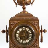 Historismus-Pendule, um 1880, Bronzeguß, 1/2-Stundenschlag auf Glocke (nicht fkt.), reich reliefiertes Gehäuse mit Amphore als Bekrönung, Pendel mit Blattfederaufhängung, reliefiertes Zifferblatt mit Emailleplaketten mit… - Foto 1