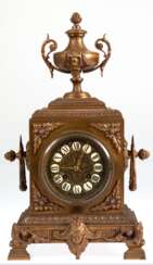Historismus-Pendule, um 1880, Bronzeguß, 1/2-Stundenschlag auf Glocke (nicht fkt.), reich reliefiertes Gehäuse mit Amphore als Bekrönung, Pendel mit Blattfederaufhängung, reliefiertes Zifferblatt mit Emailleplaketten mit…