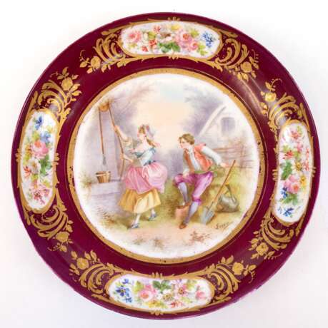 Teller, Limoges Frankreich, im Spiegel gemalte amouröse Szene, signiert, bordeauxrote Fahne mit Blumenmalerei in goldgerahmten Medaillons, etwas berieben, H. 4,5 cm, Dm. 24,5 cm - photo 1