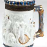 Porzellan-Bierkrug, blaue Schwertermarke in der Art von Meissen, umlaufendes Bacchanten-Relief, Asthenkel, figürlich reliefierter Deckel, z.T. mit Blaumalerei und Golddekor, fein reliefierte Zinnmontierung mit Restvergo… - Foto 1