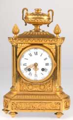Tischuhr, Frankreich um 1860, feuervergoldetes, reich reliefiertes Gehäuse mit Amphore als Bekrönung und seitl. Pinienzapfen, emailliertes Zifferblatt mit römischen und arabischen Zahlen, filigran durchbrochene Zeiger, …