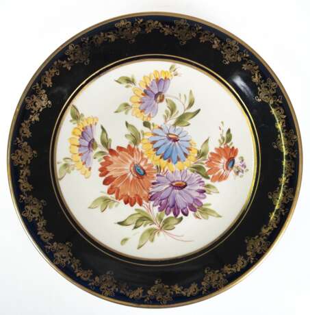 Zierteller, Weimar Porzellan, Made in GDR, mit Zusatz "Goebel Handgemalt", kobaltblaue Fahne mit reichem Golddekor, im Spiegel polychrome Blumenmalerei, Dm. 28,5 cm - фото 1 Zierteller, Weimar Porzellan, Made in GDR, mit Zusatz "Goebel Handgemalt", kobaltblaue Fahne mit reichem Golddekor, im Spiegel polychrome Blumenmalerei, Dm. 28,5 cm - фото 1