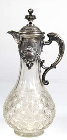 Historismus-Schenkkanne mit Silbermontur innen vergoldet (geprüft), um 1880, gebauchter Glaskorpus mit Facetten- und Baccaratschliff, reich reliefierte Silbermontur mit Scharnierdeckel und Schnabelausguß, H. 32,5 cm - photo 1 Historismus-Schenkkanne mit Silbermontur innen vergoldet (geprüft), um 1880, gebauchter Glaskorpus mit Facetten- und Baccaratschliff, reich reliefierte Silbermontur mit Scharnierdeckel und Schnabelausguß, H. 32,5 cm - photo 1