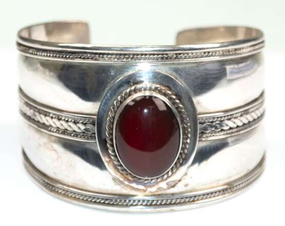 Armreif mit rotbraunem Cabochon, 928er Silber, breite offene Schien mit Kordeldekor, kl. Delle, Ges.-Gew. 34,73 g, Innen-Dm. 5,9 cm, B. 4,0 cm - photo 1