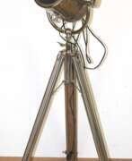 Meubles. Designer-Stehlampe in Form eines Scheinwerfers mit verstellbarem Neigungswinkel, 1-flammig, Metall, auf höhenverstellbarem Dreibein-Stativ, H. ca. 125 cm - 200 cm