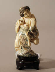 Japanese ivory netsuke showing a woman holding a baker and a bag in traditional dress, partly engraved