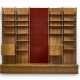 Large custom-designed bookcase made of solid wood and veneer, consisting of three bays, the central one of which is set up with a backdrop covered in red fabric, two drop-down cabinets, twenty shelves, and a base. How, 1970s. (344x300x45 cm.) (slight - фото 1