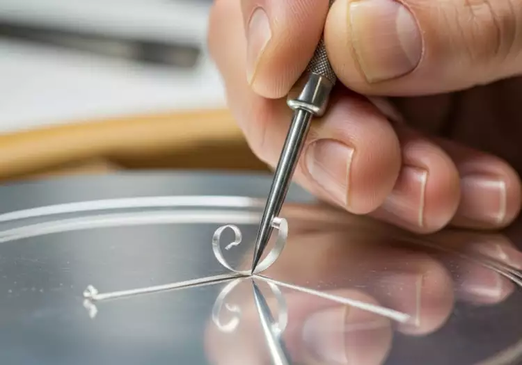 Процесс ручной гравировки - мастер с помощью штихеля наносит тонкий узор на металлическую пластину.